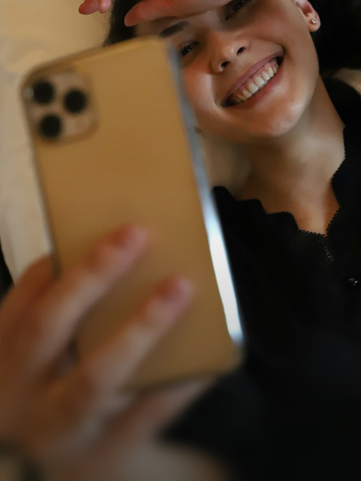 Lächelnde Person schaut auf ein goldenes Smartphone in ihrer Hand.