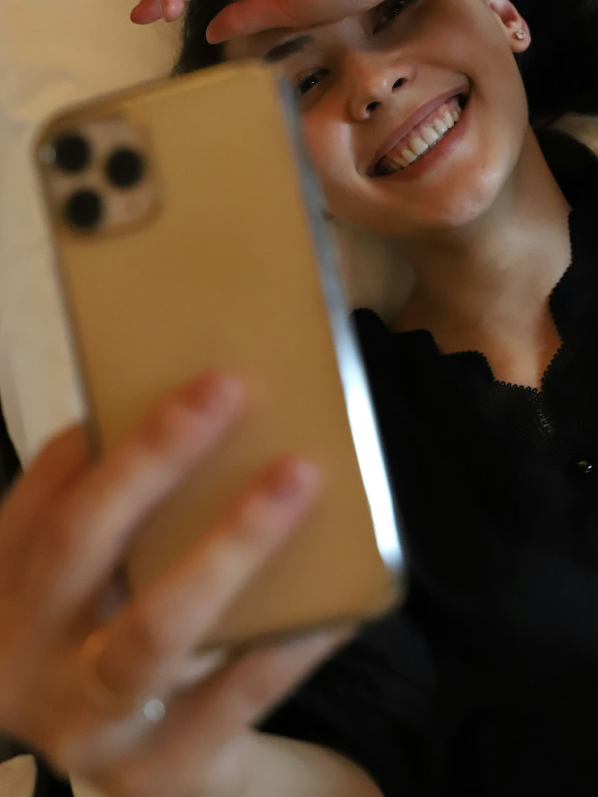 Lächelnde Person schaut auf ein goldenes Smartphone in ihrer Hand.