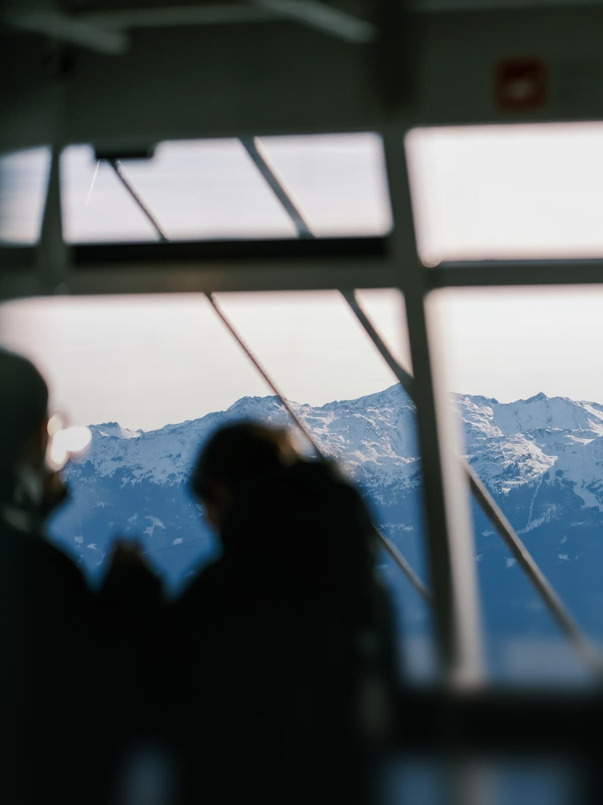 Unscharfe Silhouetten von Menschen vor einem großen Fenster mit Blick auf schneebedeckte Berge.