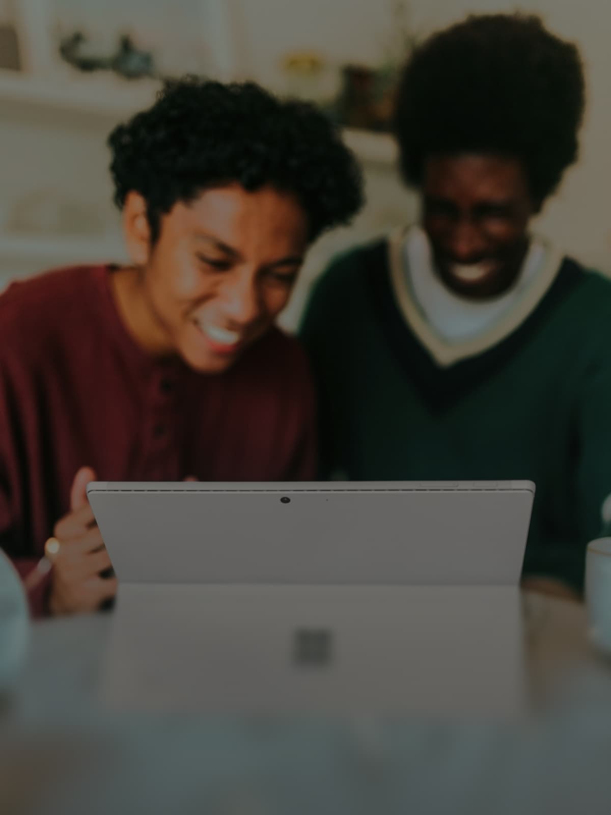 Zwei lachende Personen schauen gemeinsam auf ein Tablet auf einem Tisch.